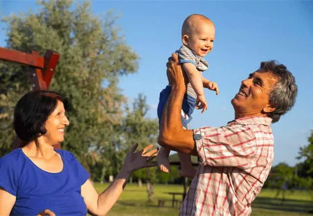 Grandparents smiling outdoors while holding their baby sized grandchild